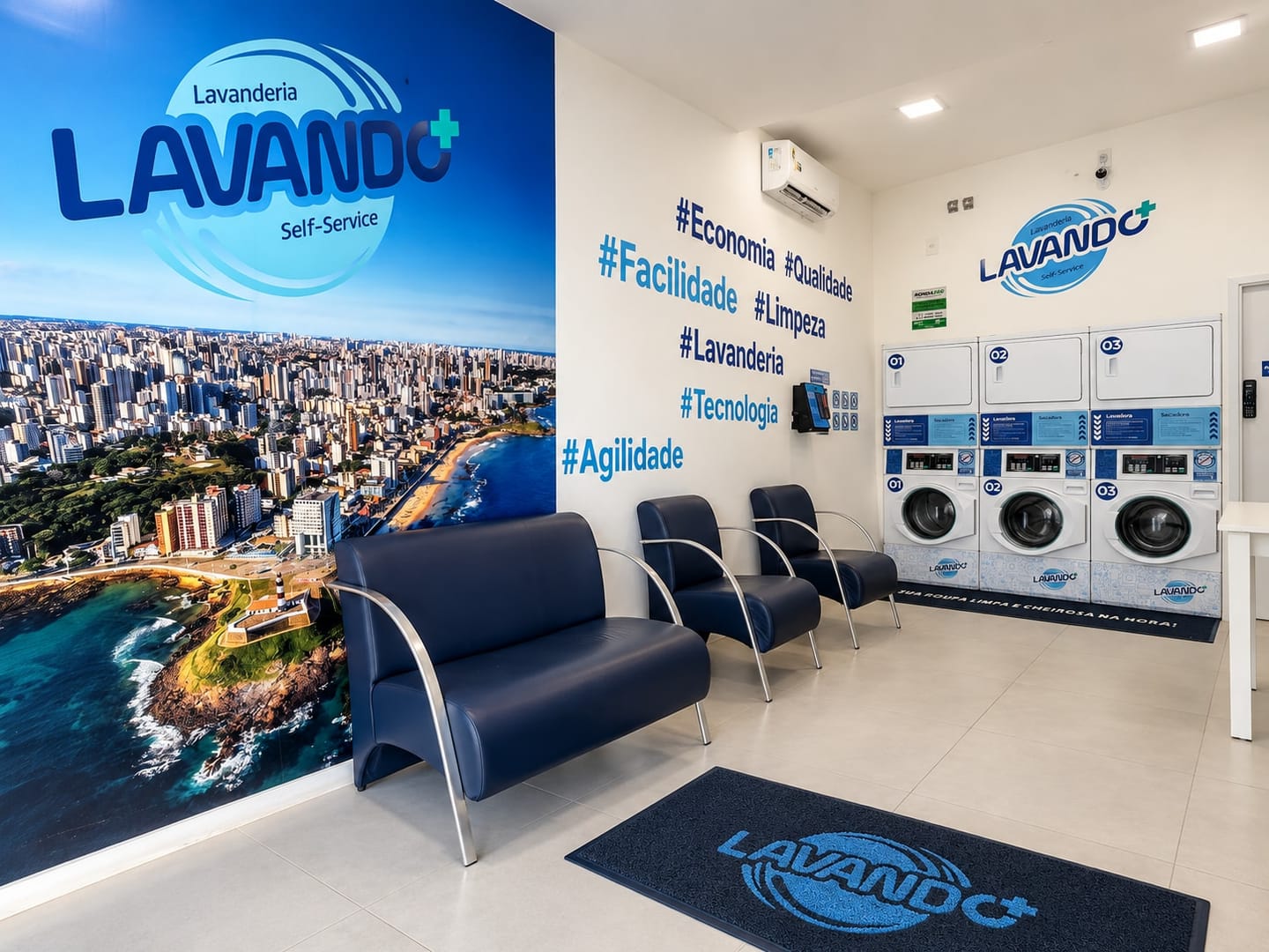 Sala de espera com poltronas azul-marinho, parede de hashtags, ar-condicionado e as três torres de lavadora ao fundo